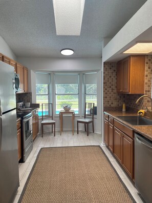 A modern kitchen with wooden cabinets, stainless steel appliances, and a large window overlooking a backyard.