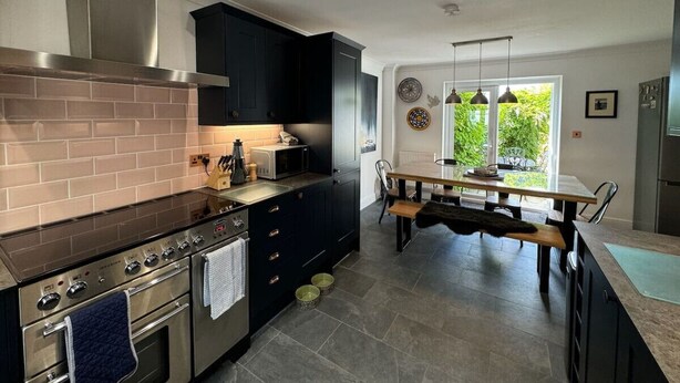 A modern kitchen with dark cabinets, a stainless steel stove, and a dining area with a wooden table and chairs.