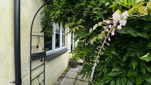 A garden entrance with a welcome sign, a black metal gate, and a potted plant.