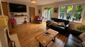 A living room with a wooden floor, a black leather sofa, a coffee table, and a TV mounted on the wall.