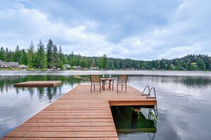 A wooden dock extending into calm water with a table and chairs, surrounded by dense forest and houses in the background. - Lakefront Snohomish Home ~ 13 Mi to Historic Dtwn (Snohomish)