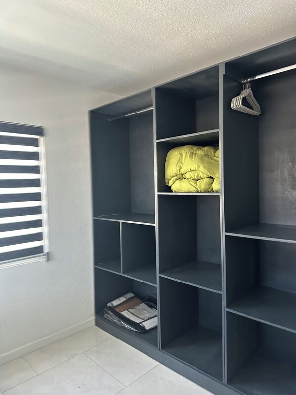 A room with a grey built-in wardrobe, a window with horizontal blinds, and a tiled floor.