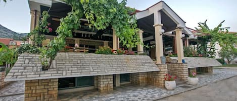 A modern building with a stone facade, covered patio, and a garden area with flowers.