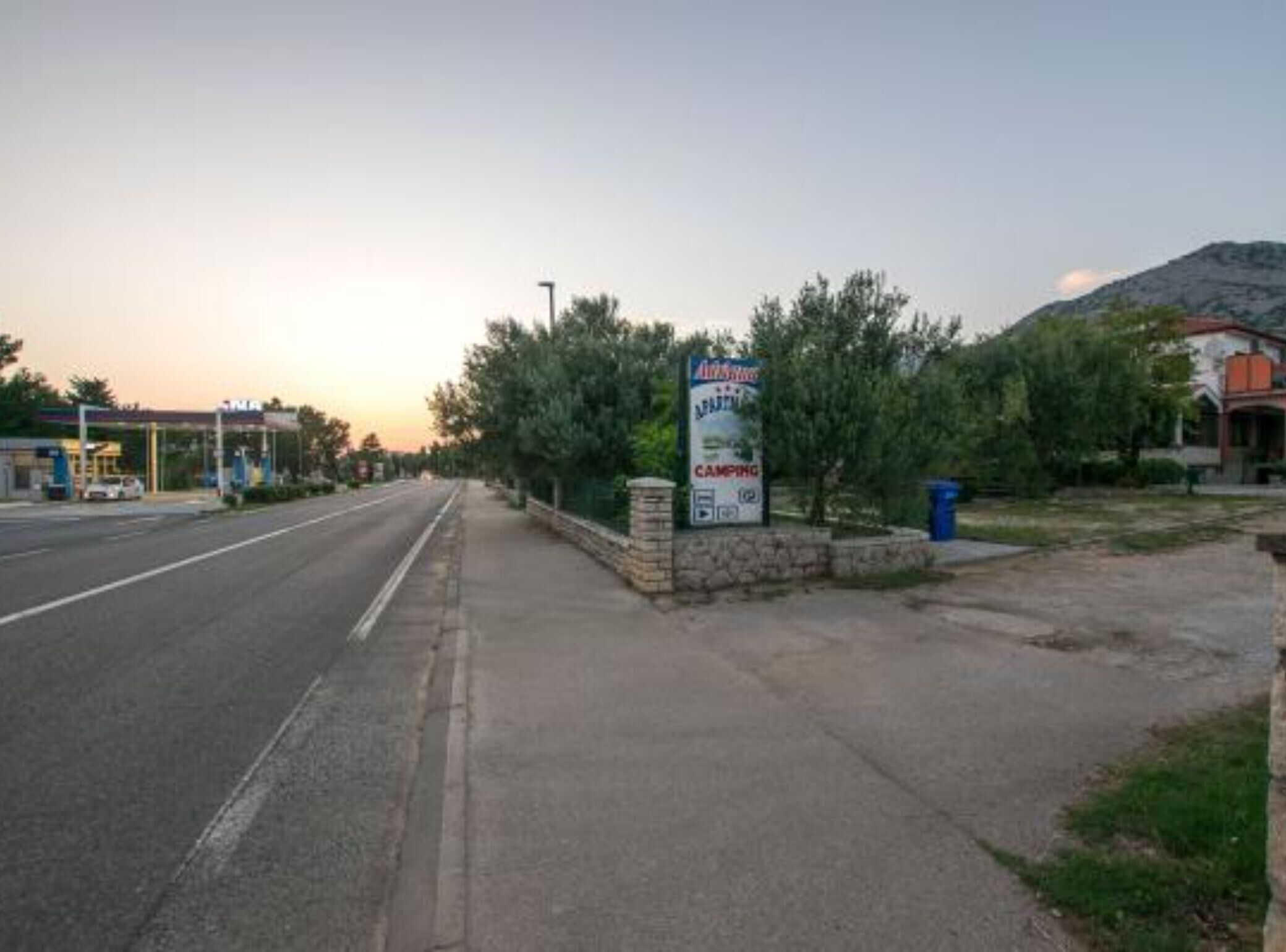 Una carretera con un cartel de camping, una gasolinera y un edificio al fondo.