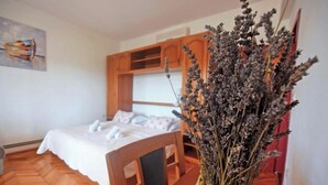 Un dormitorio con una cama de madera, una mesita de noche, un florero con flores secas y un cuadro en la pared.