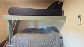 Una cama litera con escalera, un termostato fijado a la pared y una pequeña alfombra en el suelo.