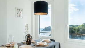 A dining table set with plates, glasses, and a vase with flowers, overlooking a scenic coastal view. - Magic Seaside Apartment (Rosignano Marittimo)