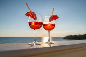 Two glasses of red beverage with fruit garnish on a seaside balcony. - Magic Seaside Apartment (Rosignano Marittimo)