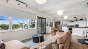 A modern living room with a sofa, a glass coffee table, and a dining area with chairs. - Ocean View Skenes Creek Beach House (Skenes Creek)