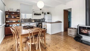 A modern kitchen with white cabinets, a central island, and a wood-burning stove. - Ocean View Skenes Creek Beach House (Skenes Creek)