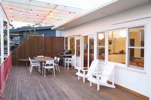 A covered outdoor patio with a grill, white chairs, and a table.