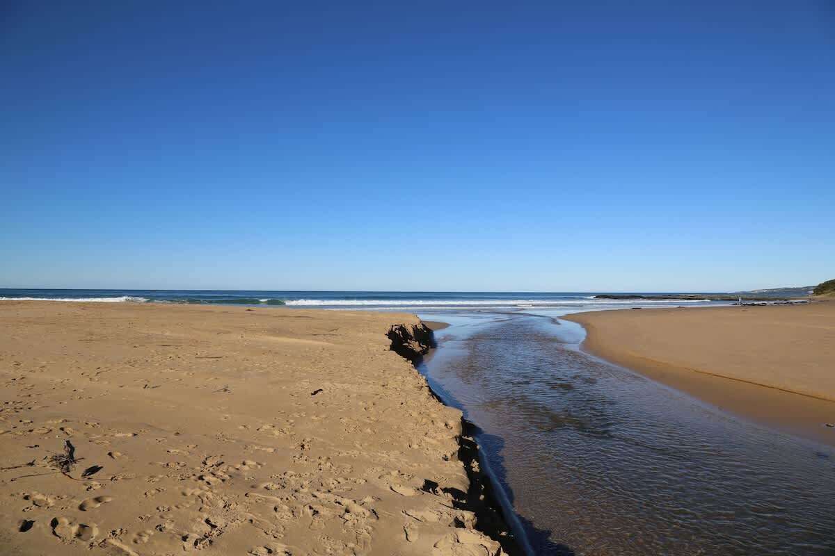Une plage avec un ciel dégagé, un rivage sablonneux et un promontoire rocheux.