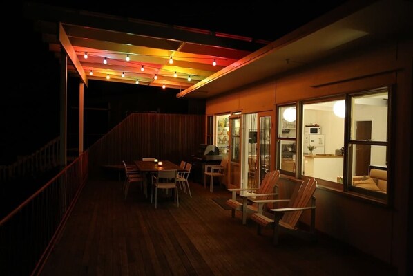 A covered outdoor area with a dining table and chairs, a grill, and a view into the house through glass doors.