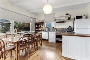 A kitchen with a dining table, chairs, a refrigerator, a stove, and a hanging light fixture.
