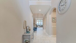 A spacious hallway with a high ceiling, a clock on the wall, and a staircase leading to an upper level.