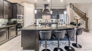 A modern kitchen with dark cabinetry, a central island with bar stools, and a staircase leading to an upper level.