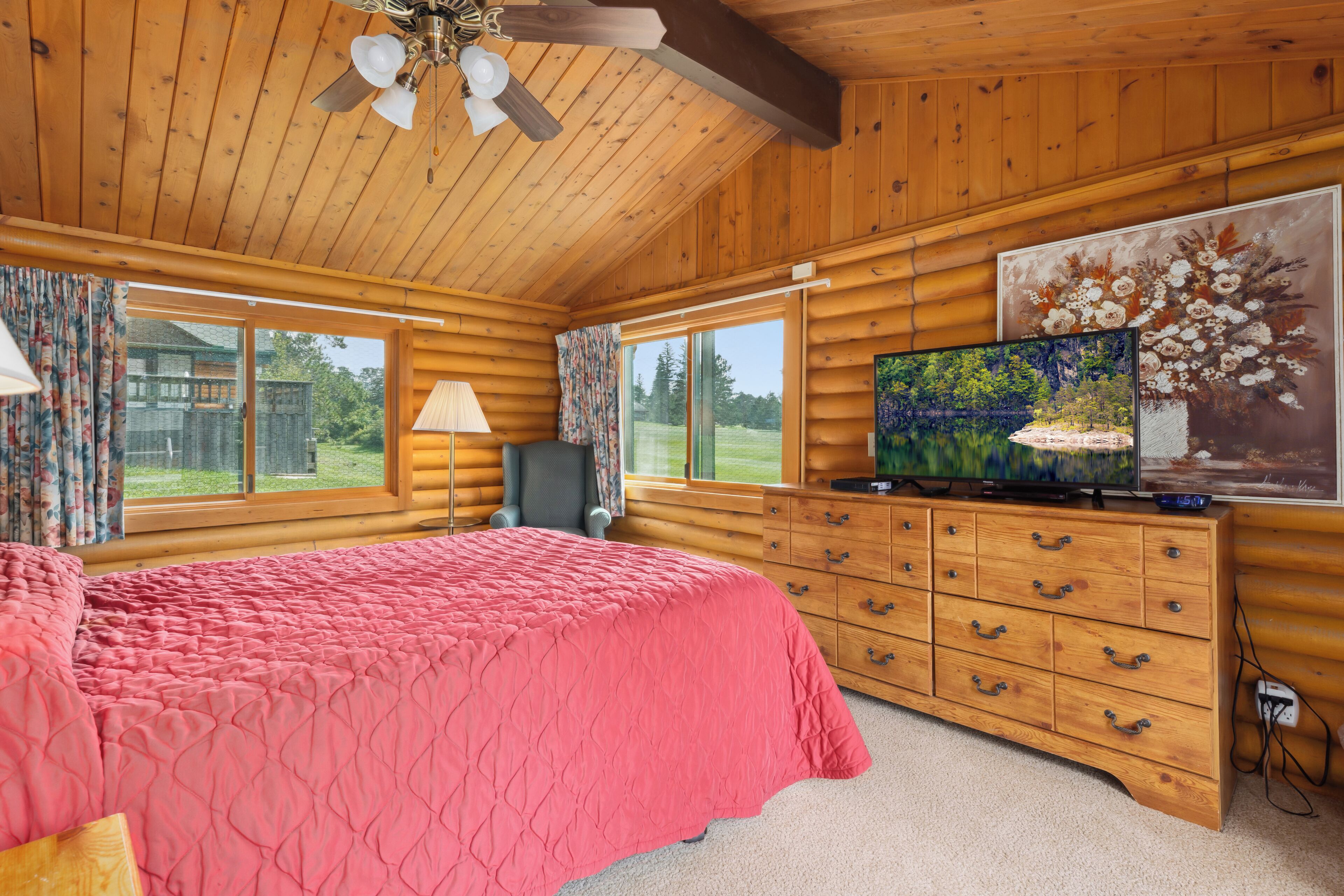 Une chambre située dans une cabane en rondins, avec un grand lit, une commode en bois et un téléviseur.