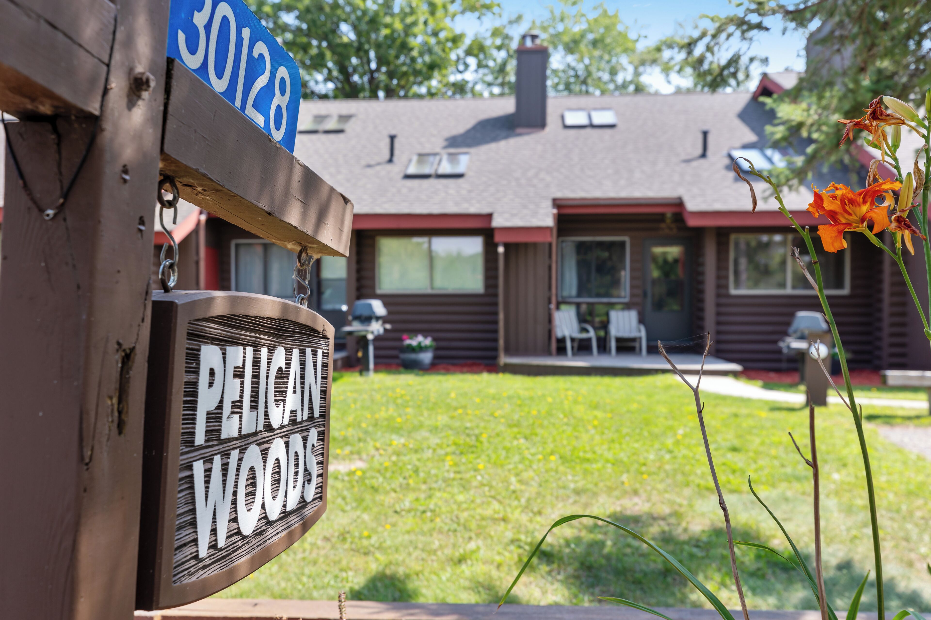A wooden mailbox with a house number sign and a 'PELIGAN WOODS' sign.