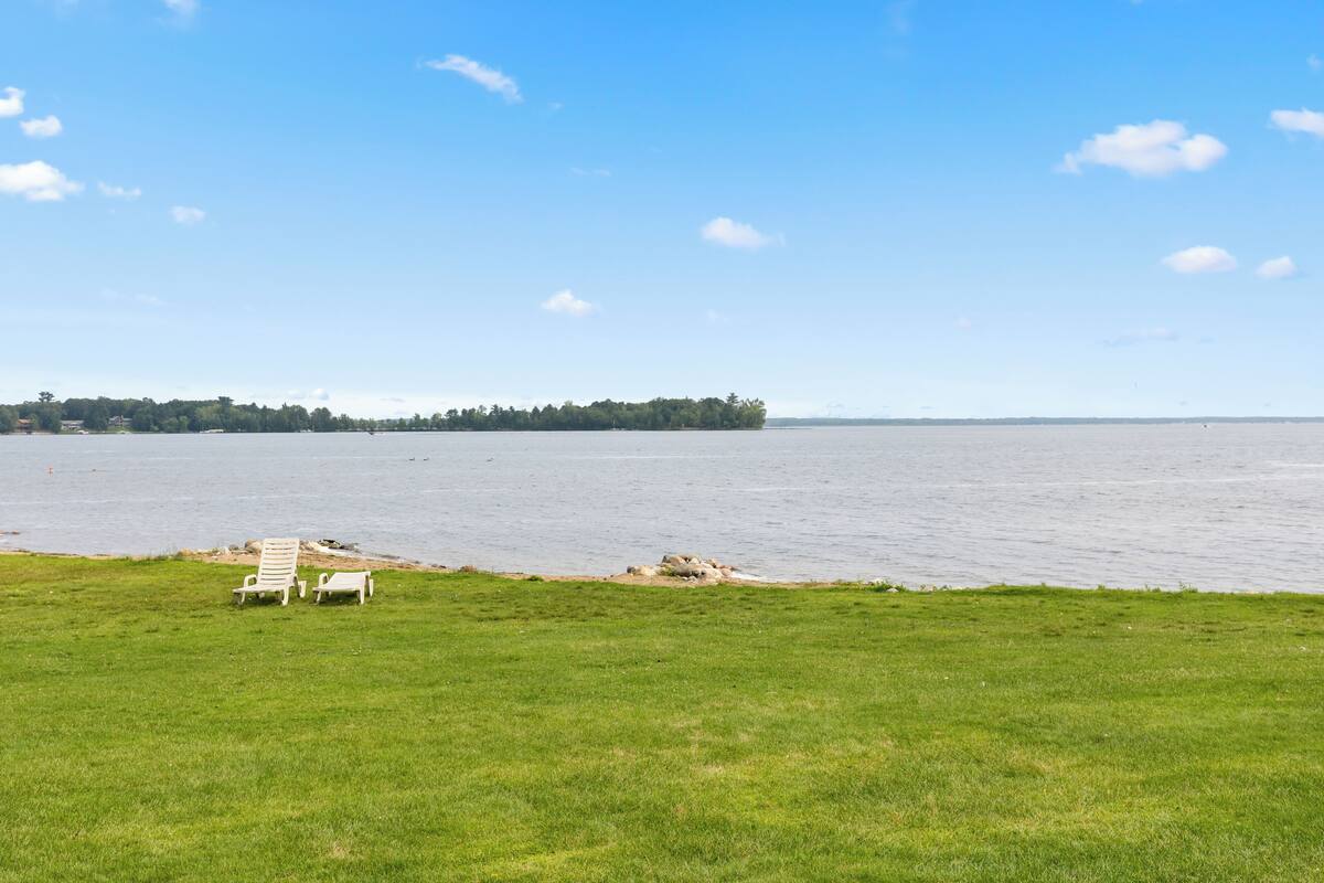 A grassy area with two white lounge chairs facing a calm body of water.