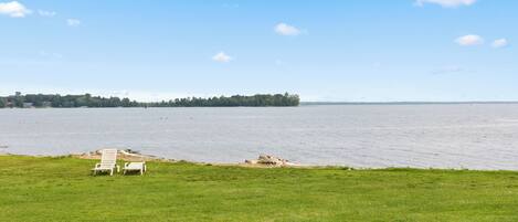 A grassy area with two white lounge chairs facing a calm body of water.
