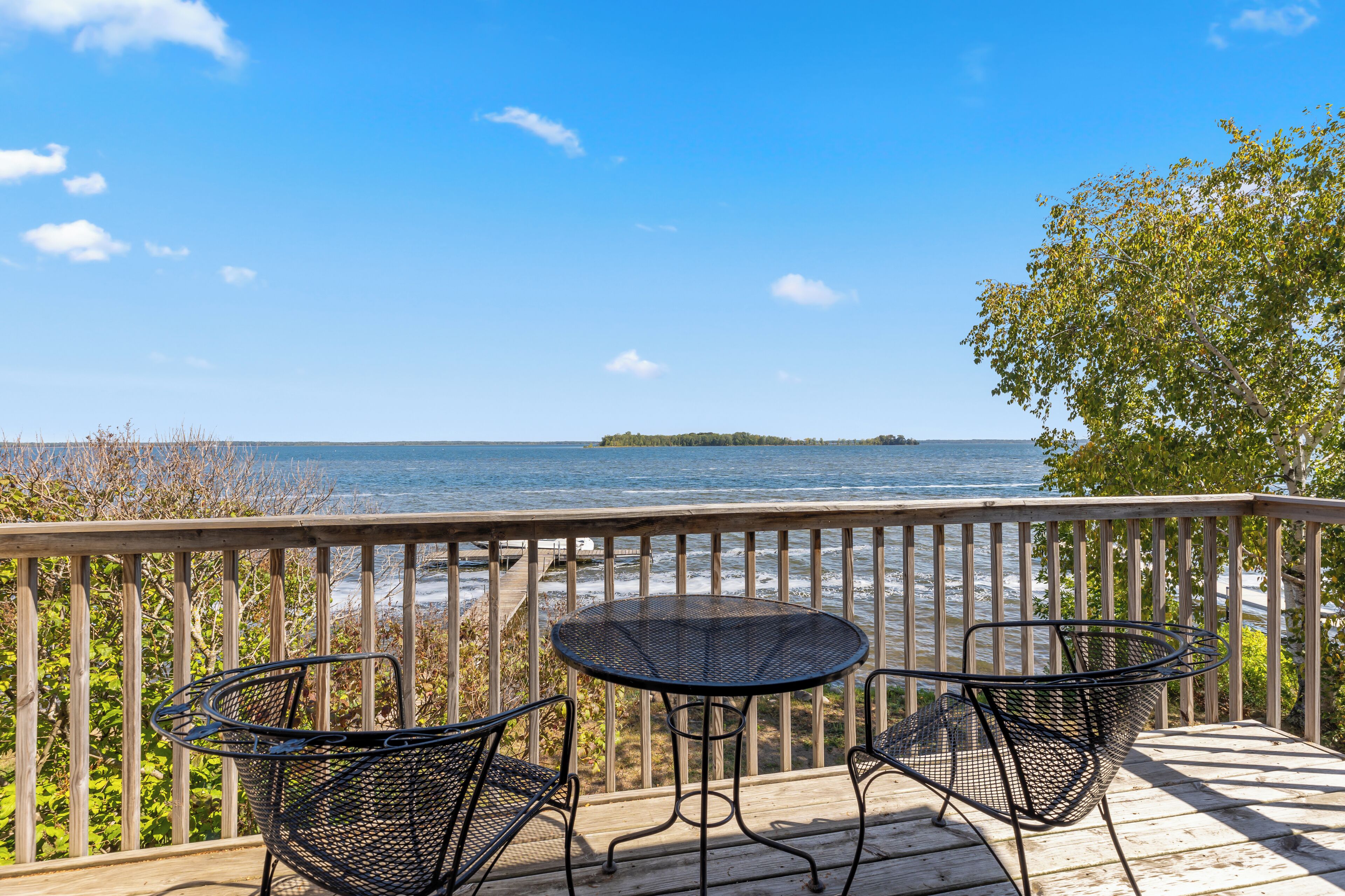 A wooden deck with a table and two chairs overlooking a beach and a distant island.