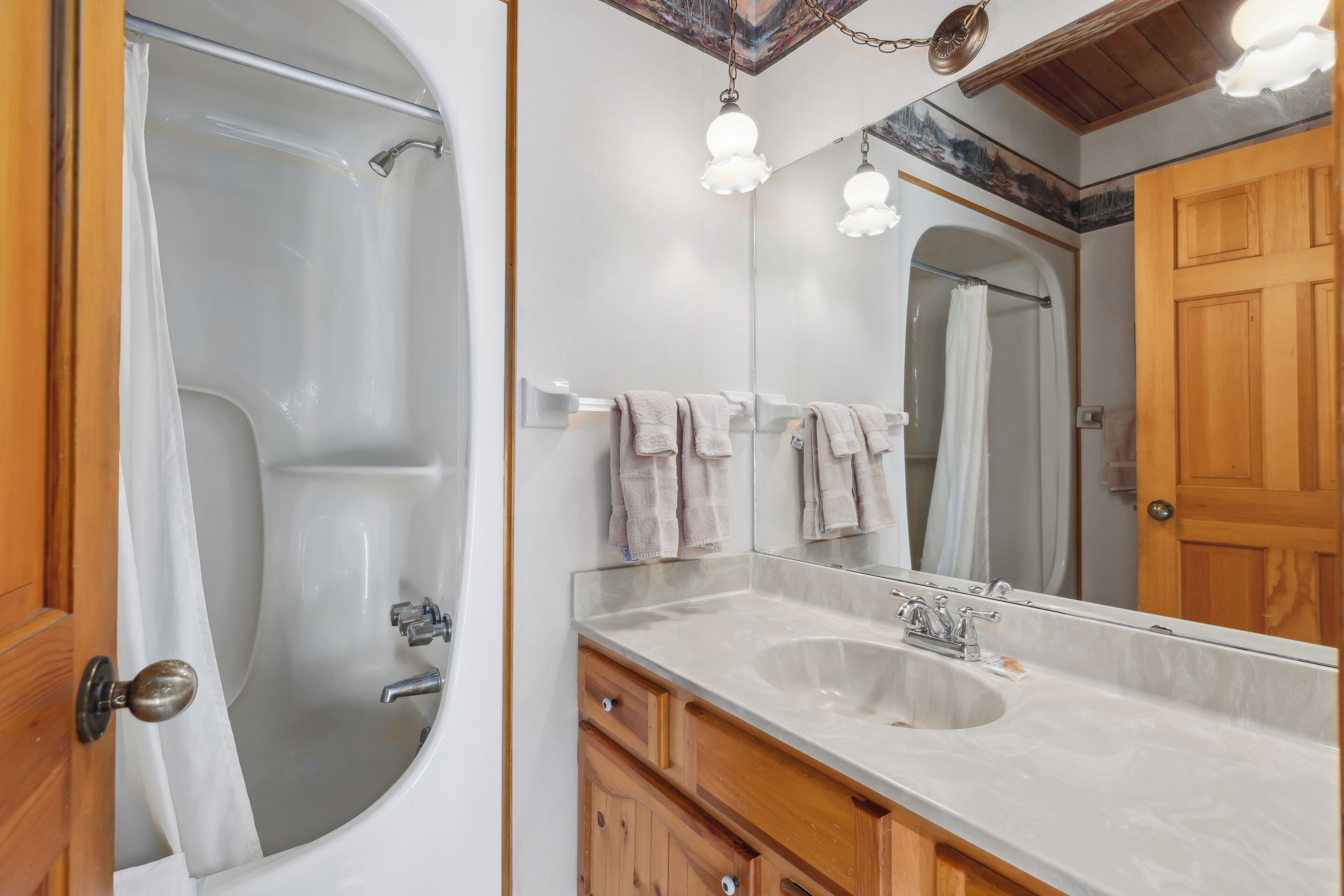 A bathroom with a bathtub, a sink, a mirror, and wooden cabinets.