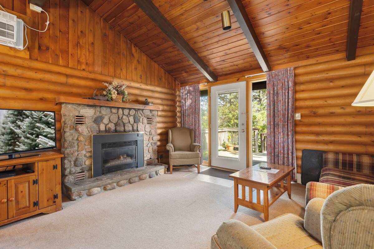 A cozy cabin interior with a stone fireplace, wooden walls, a television, and a comfortable seating area.
