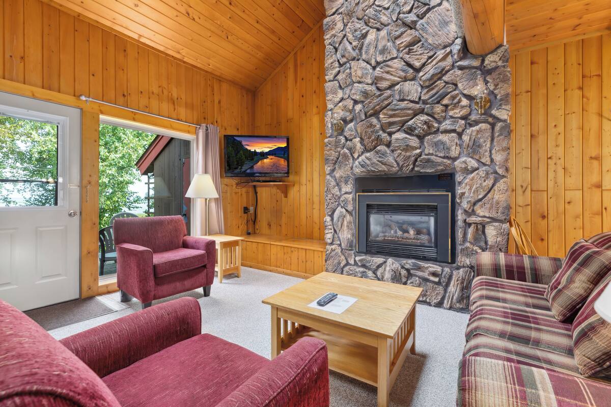 A cozy cabin interior with a stone fireplace, wooden walls, and a television mounted on the wall.