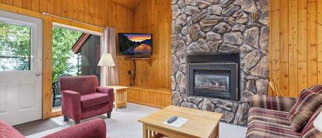 Un acogedor interior de cabaña con chimenea de piedra, paredes de madera y un televisor montado en la pared.