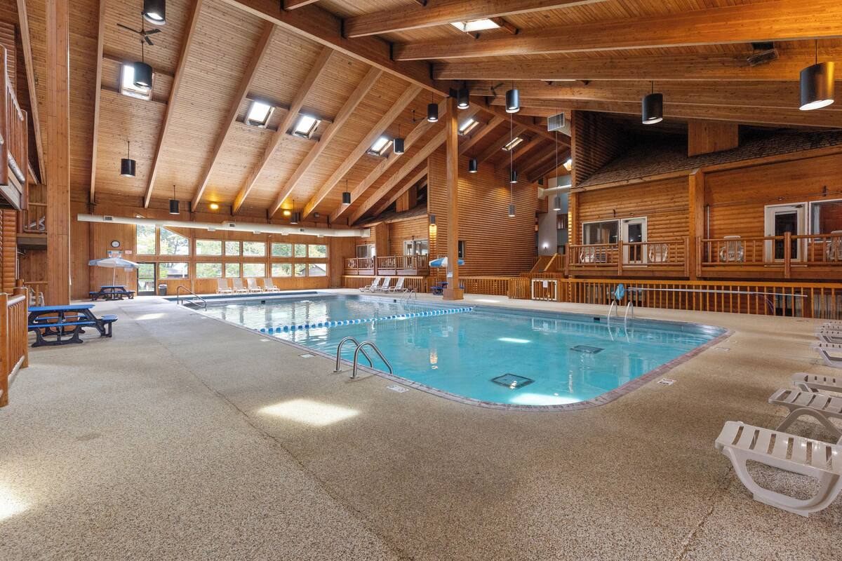 An indoor swimming pool with wooden beams, a pool ladder, and lounge chairs.