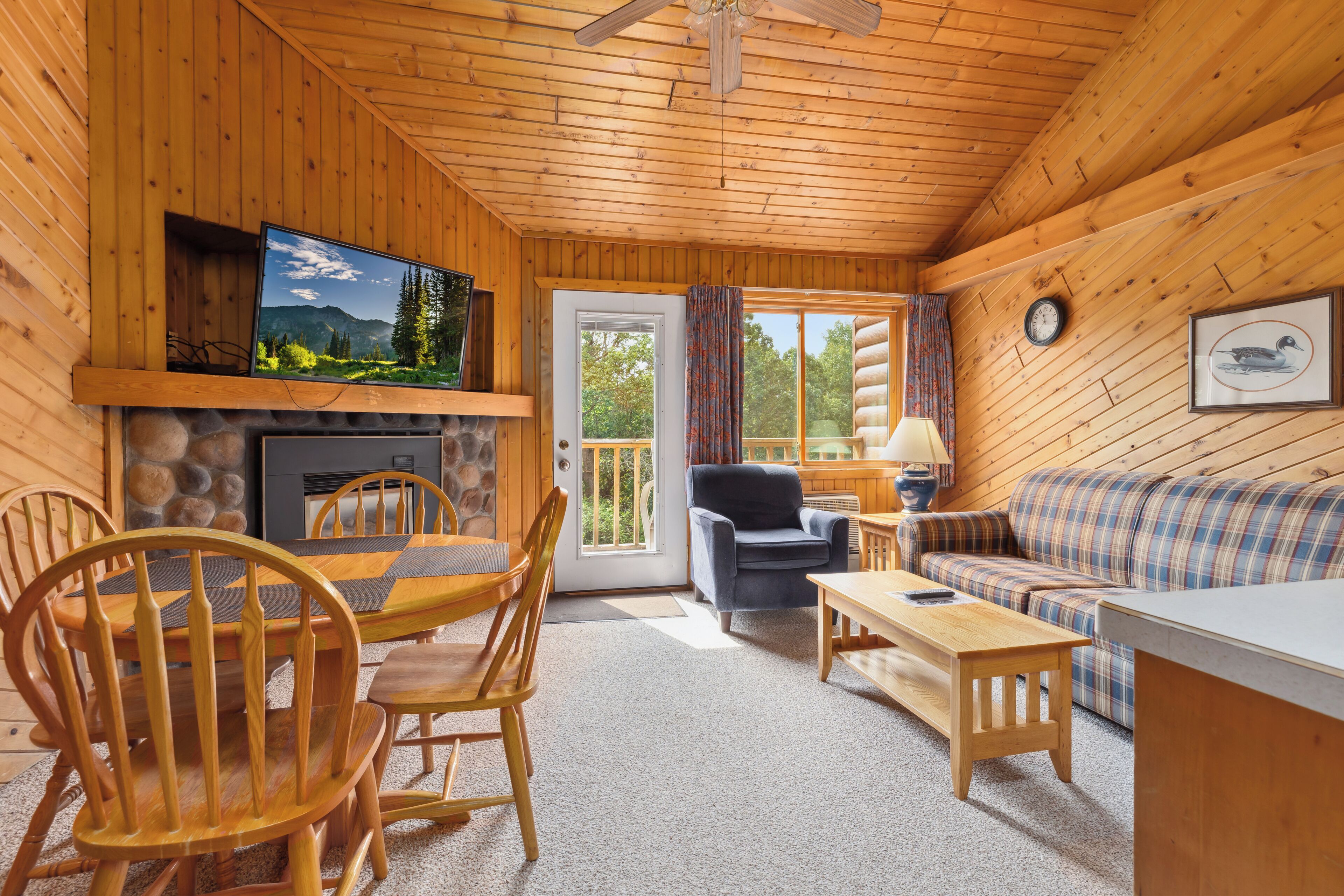 A log cabin interior with a stone fireplace, wooden dining table, and a sofa.