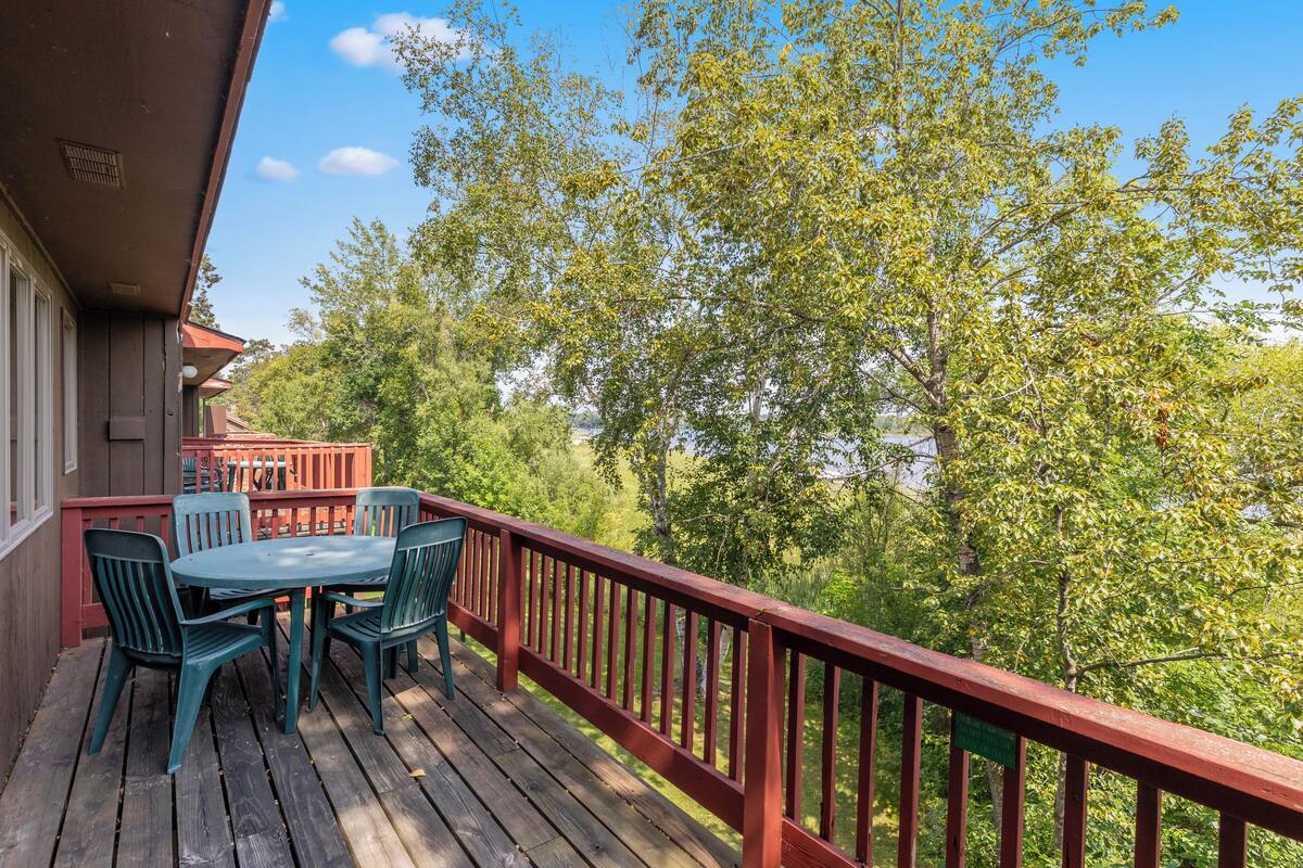 A wooden deck with a red railing, a table, and chairs.