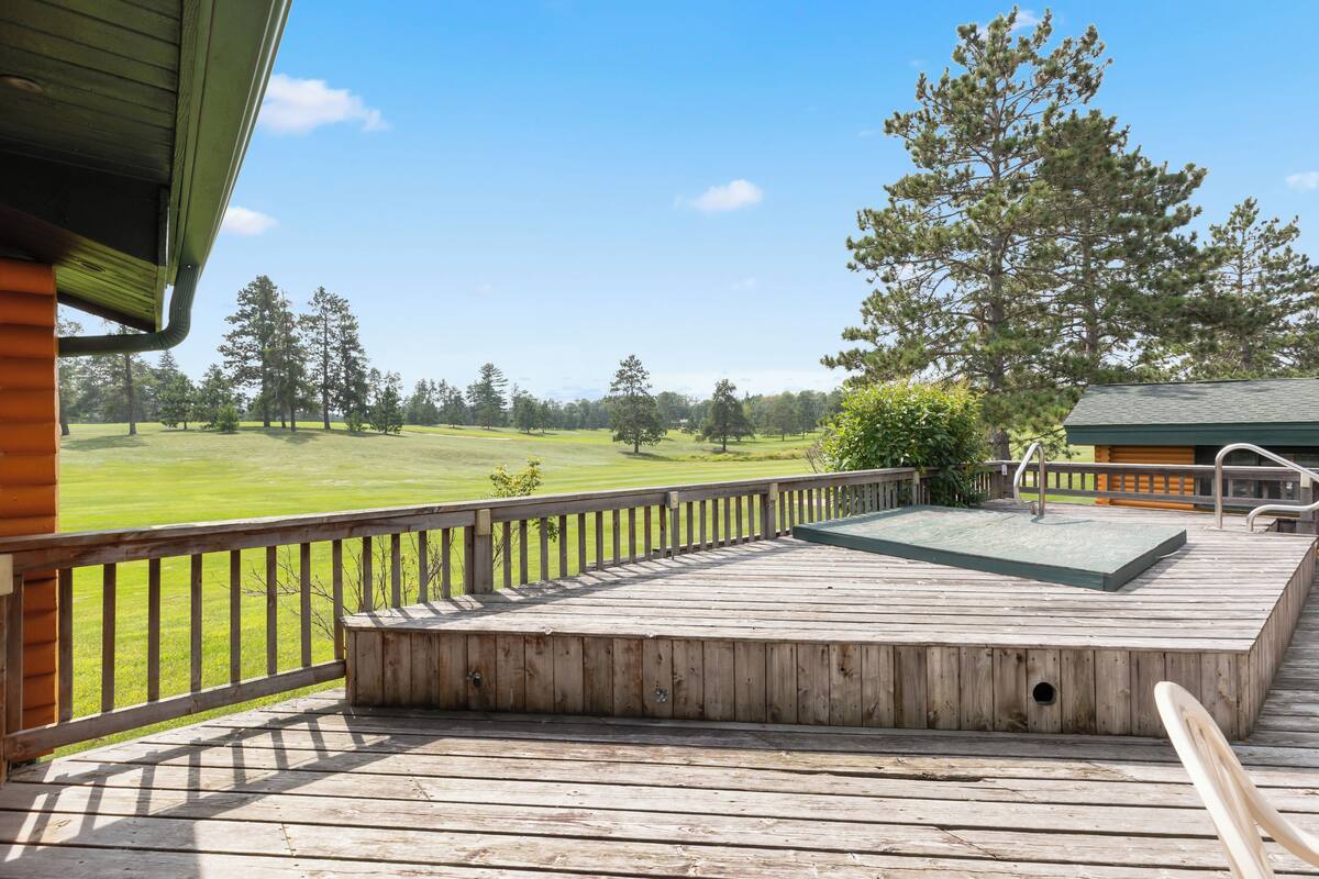 A wooden deck with a view of a green field and trees.
