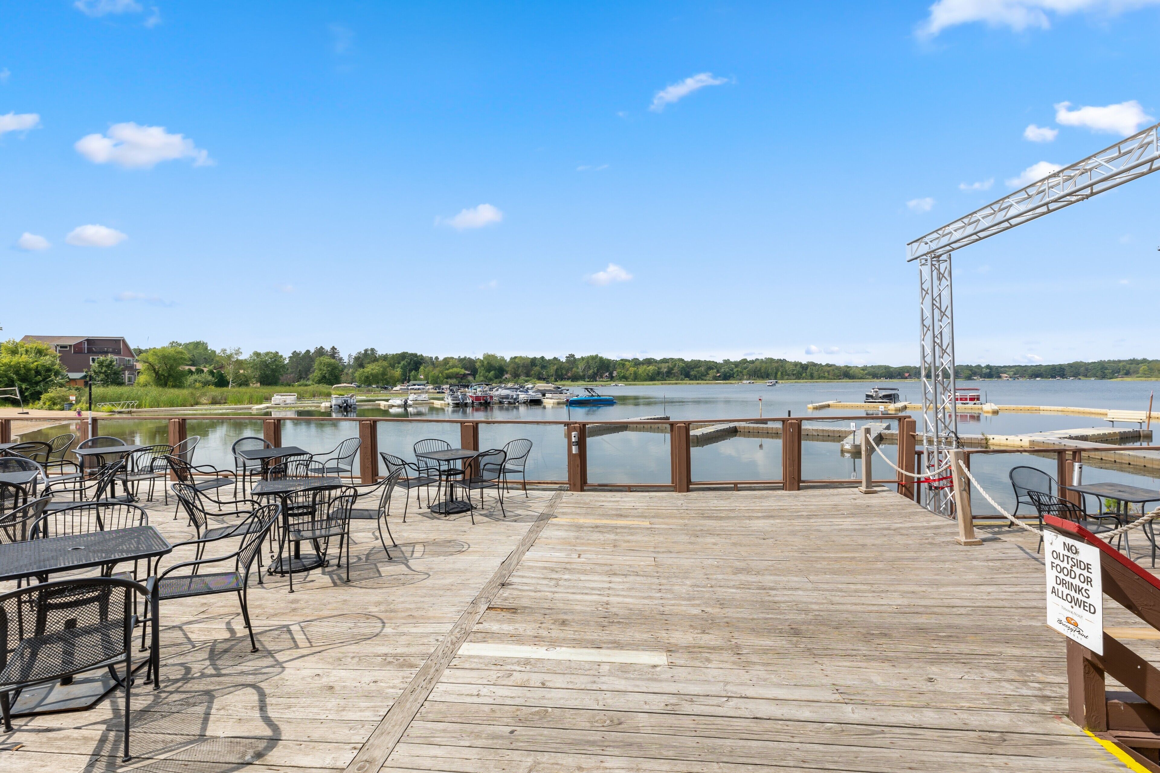 A wooden deck with tables and chairs overlooking a body of water with boats.