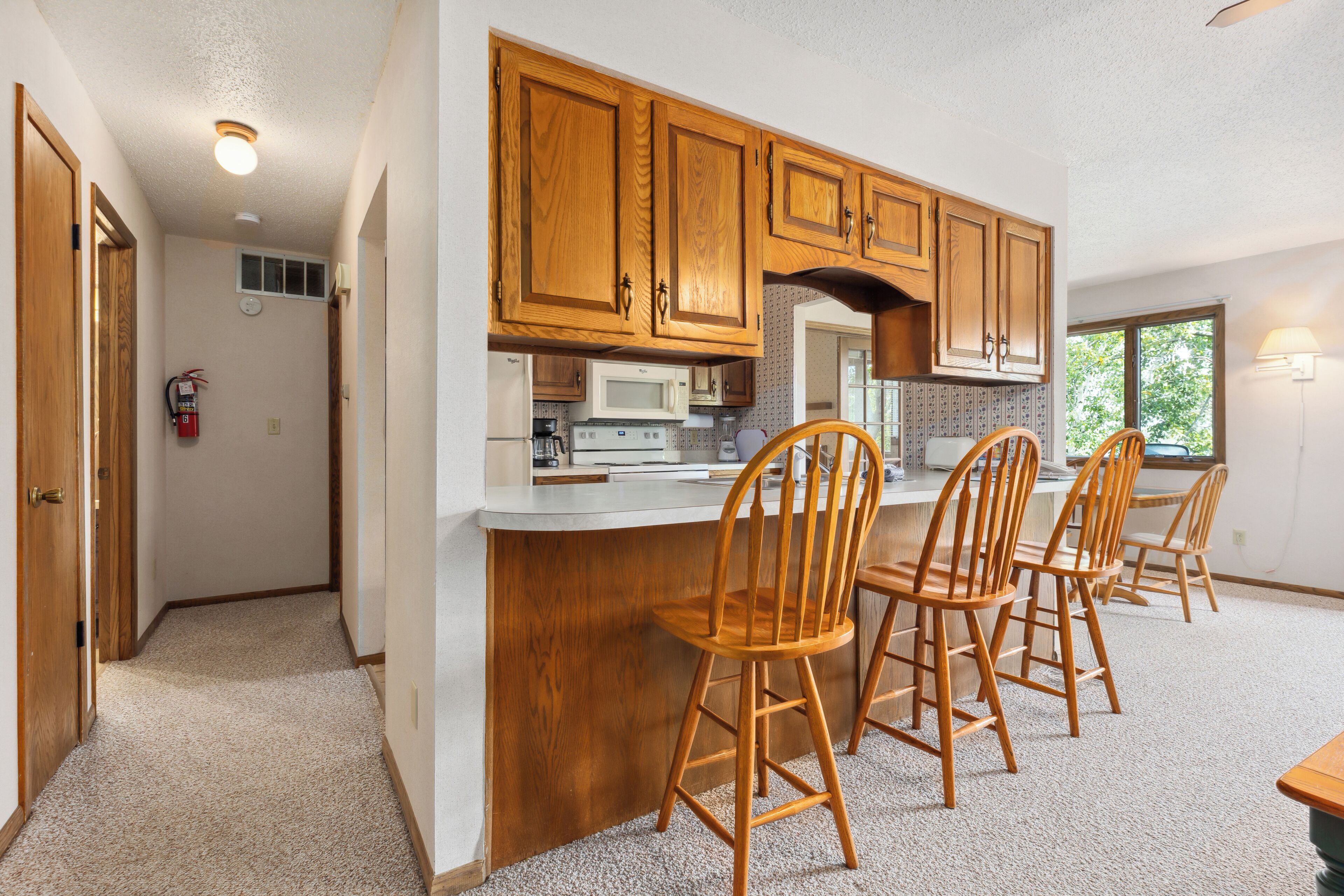 A kitchen with wooden cabinets, a microwave, and a bar area with four wooden chairs.