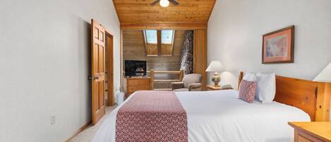 Een slaapkamer met een houten plafond, een bed met een geborduurde sprei, een nachtkastje, een stoel en een schilderij aan de muur.
