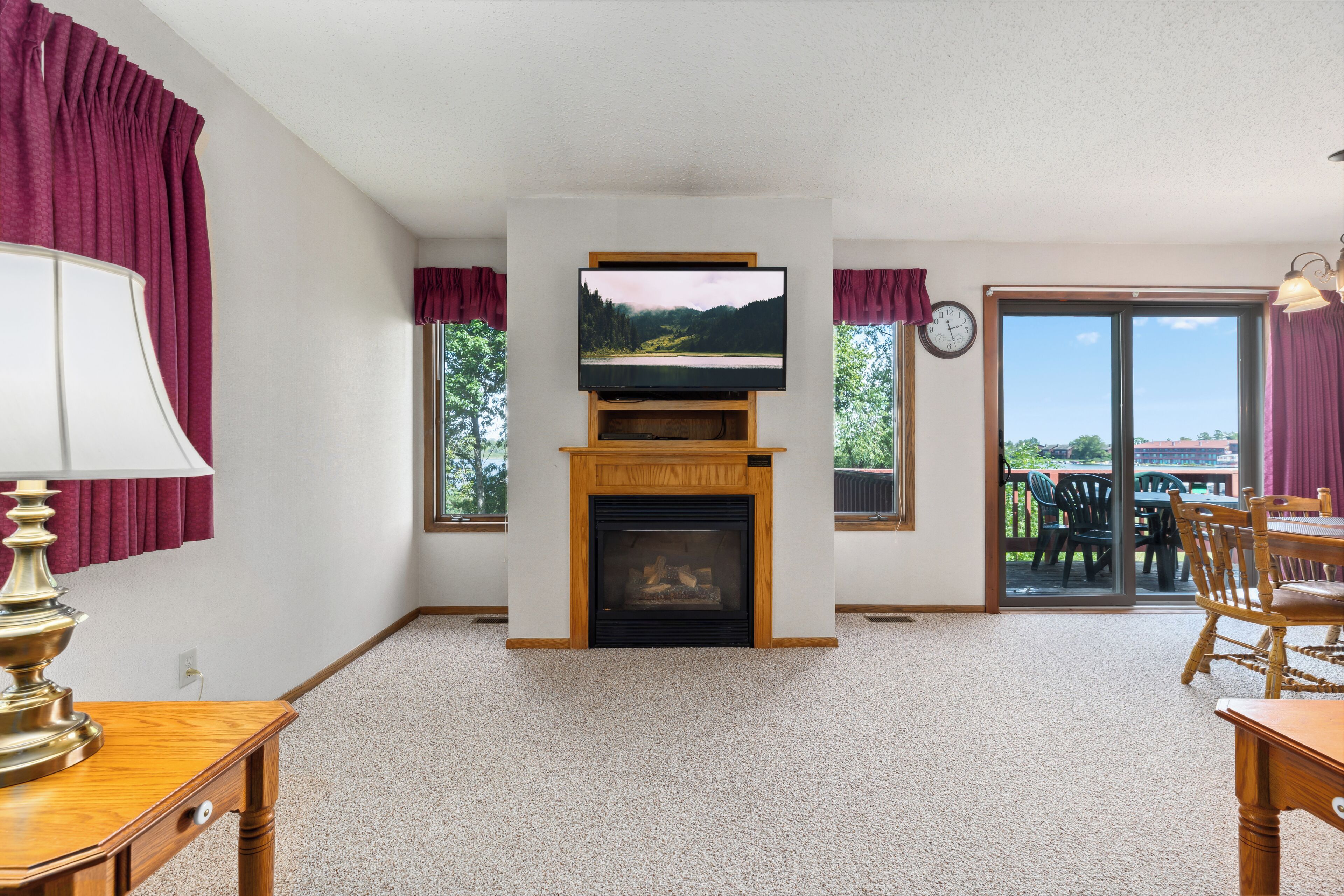 A living room with a fireplace, a television mounted above it, and a view through the glass door to the outside.