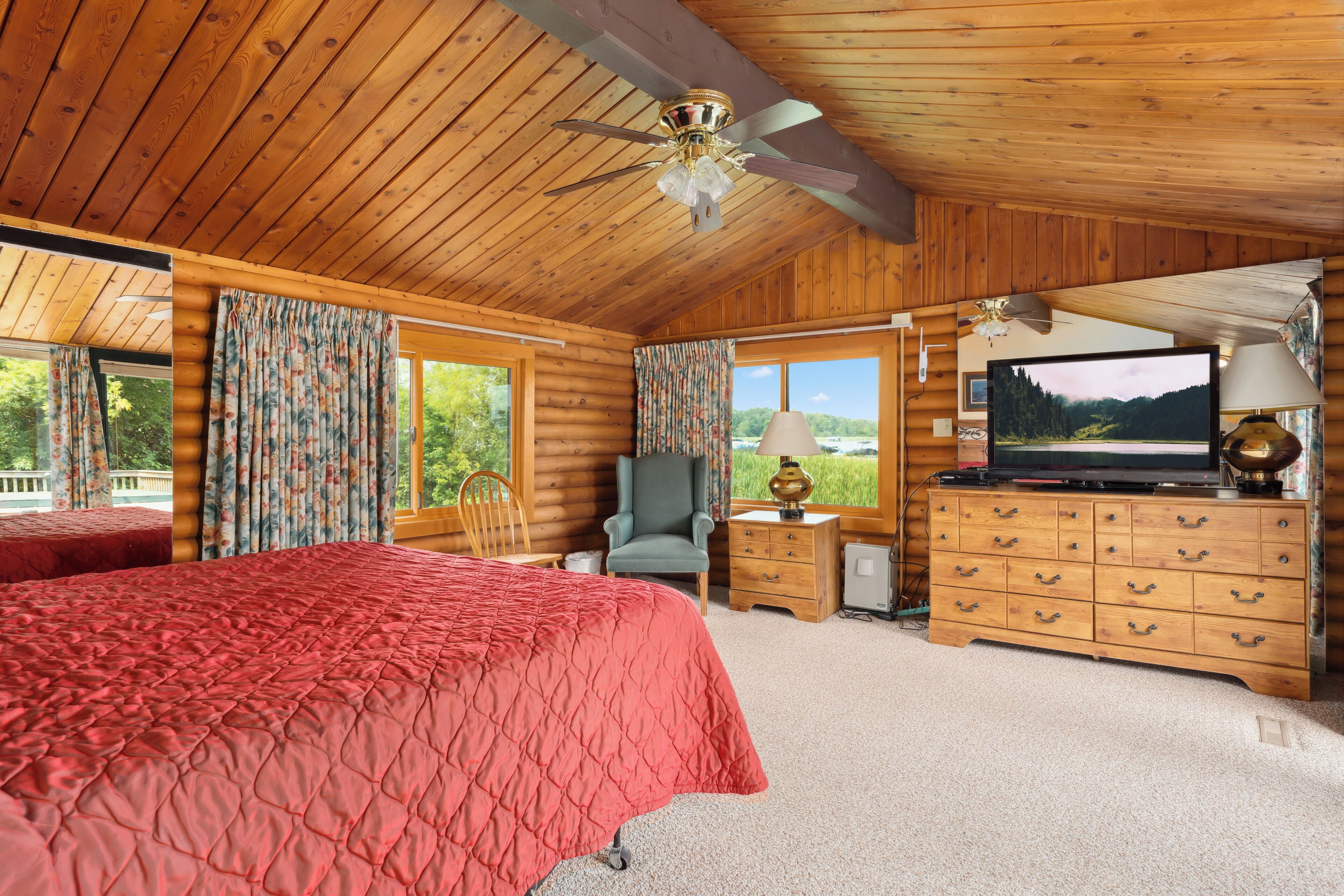 Een slaapkamer in een blokhut met een groot bed, een televisie, een dressoir en een stoel.