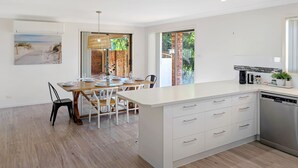 Una cocina moderna con armarios blancos, una isla grande y un comedor con mesa y sillas de madera.