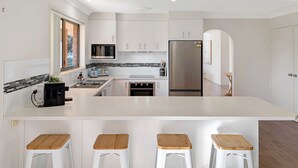 Una cocina moderna con armarios blancos, una isla central con taburetes, horno empotrado y refrigerador.