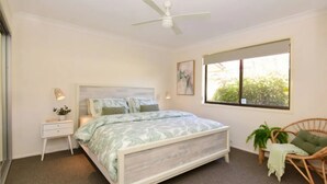 Un dormitorio con cama, mesitas de noche, ventilador de techo, ventana con vistas y una silla.