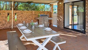 Un patio al aire libre con pared de ladrillo, una parrilla y una mesa lista para comer.