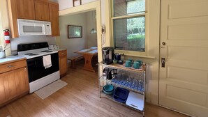 Una cuina amb armaris de fusta, microones, fogó i finestra amb vista a vegetació.