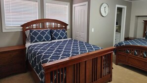 Een slaapkamer met twee houten bedden, een witte deur, een klok aan de muur en een raam met zonwering.