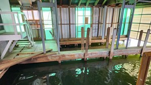 Een houten steiger over het water, met een metalen hekwerk en een overdekt gedeelte met ramen.