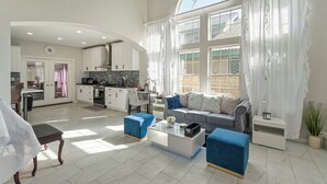 A spacious living area with a sofa, ottomans, and a coffee table. A kitchen is visible in the background with a dining area. - 6 bedroom Large house. Near Airport,Outlets Mall, No Party, Pets Friendly (Ontario)