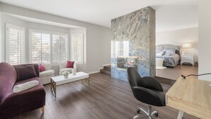 A modern living room with a sofa, a coffee table, and a black chair. There is a large marble accent wall and a bed with a nightstand in the background. - 6 bedroom Large house. Near Airport,Outlets Mall, No Party, Pets Friendly (Ontario)