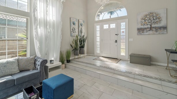 A spacious living room with a grey sofa, a blue ottoman, and a large window with sheer curtains. - 6 bedroom Large house. Near Airport,Outlets Mall, No Party, Pets Friendly (Ontario)
