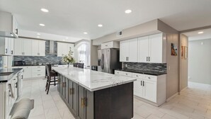 A modern kitchen with white cabinets, a marble island, and stainless steel appliances. - 6 bedroom Large house. Near Airport,Outlets Mall, No Party, Pets Friendly (Ontario)