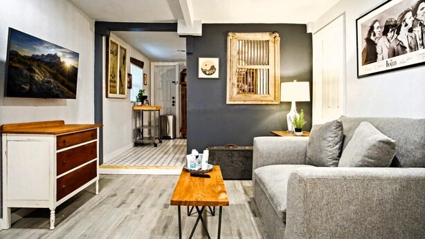 A modern living room with a grey sofa, wooden coffee table, and a white dresser. A framed picture of the Beatles hangs on the wall, and a window with a wooden frame is visible. - Harmony Studio 5min-asian Dist Full Kitchen (Oklahoma City)